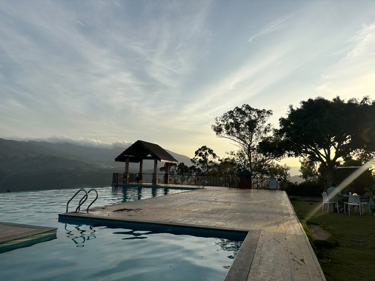 An infinity pool merges with misty hill country mountains under a glowing dusk sky.