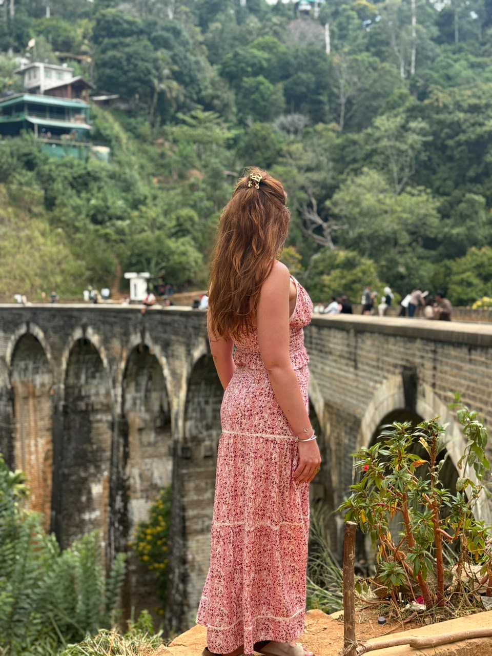 A traveler in a flowing floral dress admires the iconic Nine Arch Bridge amid lush Ella greenery.