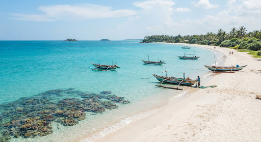 Turquoise shallow waters and powdery white sand beach of Pasikuda and Nilaveli in Trincomalee Sri Lanka with wooden outrigger boats, coral reefs visible under crystal ocean, bright summer sunshine and tranquil tropical serenity.